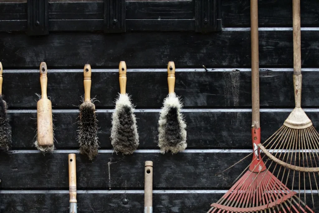 Hand brushes and rakes hanging on a dark timber shed wall