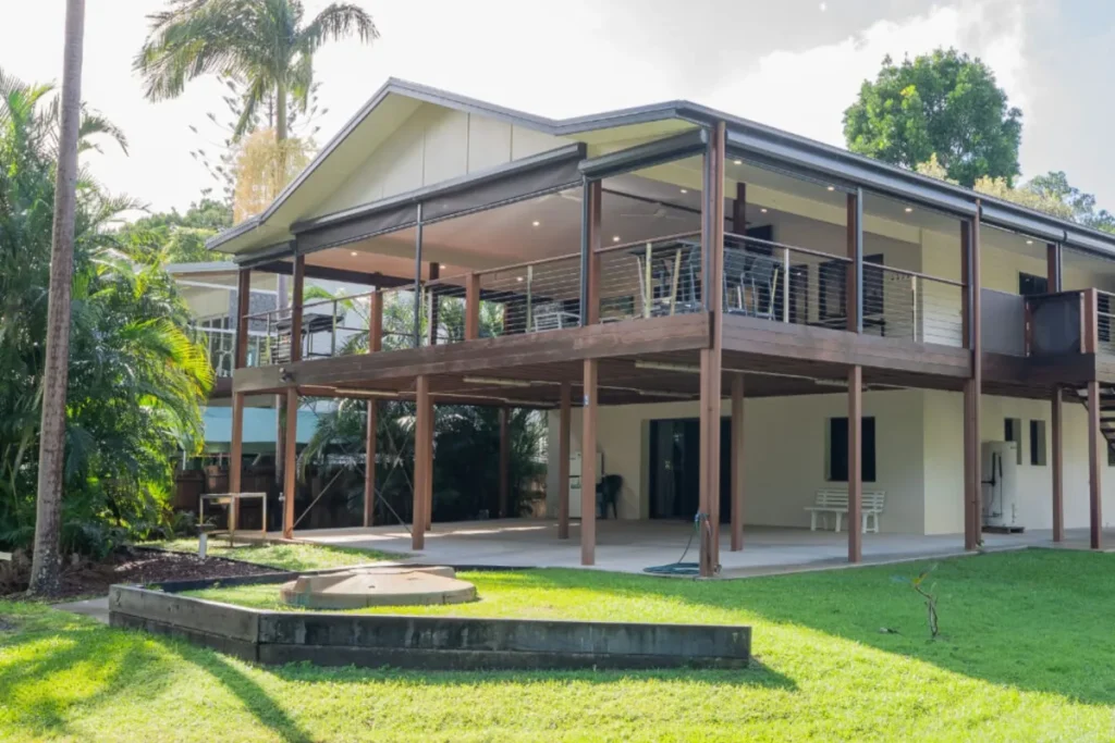 Elevated timber house with a wide deck, lawn and palm trees