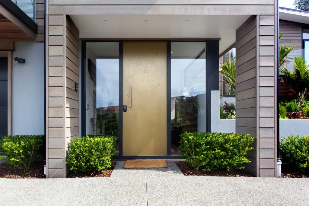 Modern front entrance with a bronze door, glass side panels and hedges