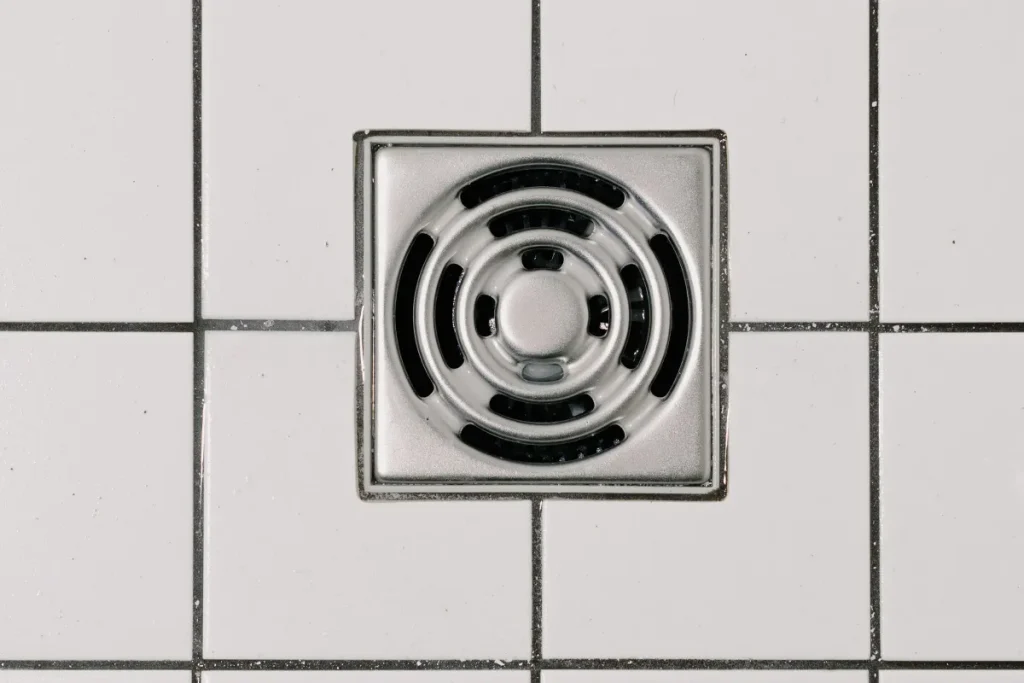 Stainless steel floor drain set in white shower tiles