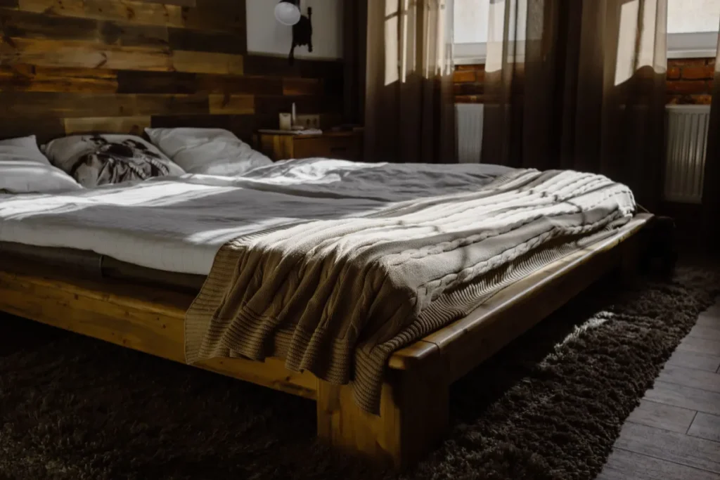 Low wooden bed frame with a mattress and knitted throw in a dim bedroom